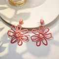 Detail of pink hand-woven raffia flower earrings placed on white ceramic plate edges - Pink