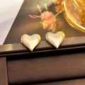Macro shot of polished gold heart stud earrings on a dark jewelry display stand - 44# Nude Heart Studs