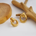 Close-up of golden triple-interlocked geometric hoop earrings on a minimalist wooden base - Triple Intertwined Circles