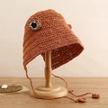 Dettaglio cappello da sole arancione intrecciato a mano con occhi decorativi e cordino - Arancione