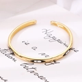 Macro view of a gold-plated C-shaped cuff bracelet featuring black enamel evil eye motifs. - Black