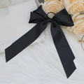 Detail of elegant black satin bow hair clip with long streamers on white plush surface - Black