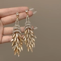 Gros plan de boucles d'oreilles pendantes en strass avec cristaux champagne et dorés - Style Plume et Gland / Brun doré