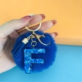 Close-up of blue pompom keychain with sequined letter F resin pendant and gold clasp - Letter F