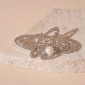 Primer plano detallado de un broche Saturno plateado con circonitas y perla sobre piedra - Broche de Planeta Saturno Plateado