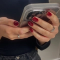 Close-up of deep red glossy press-on nails on model holding a phone with silver rings - Medium Square / Brick Red