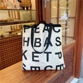 Große Canvas-Tragetasche mit schwarzem Buchstabendruck auf einer hölzernen Bäckerei-Theke - Schulter + Handtasche Cremeweiß