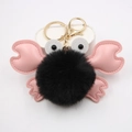 Close-up of a crab-shaped keychain featuring a black pompom with pink faux leather claws - Black