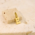 Macro shot of a polished golden letter E pendant on a textured beige stone surface - Letter-E / Steel