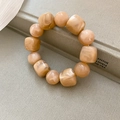 Detail view of amber acrylic bracelet with irregular square beads on textured book background - Light Coffee