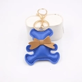 Blue PU leather bear keychain with brown bow on a minimalist white pedestal display - Sapphire Blue