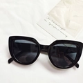 Occhiali da sole cat-eye neri con lenti scure su sfondo in tessuto bianco minimalista - Nero