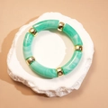 Détail de tubes en résine marbrée verte et perles dorées sur pierre texturée - Forme de Nœud de Bambou / Vert