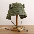 Dettaglio cappello a rana verde per bambini con occhi e laccetti su supporto di legno - Verde Scuro