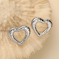 Macro view of silver heart stud earrings with dot texture on beige coral background - Silver