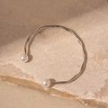Eleganter silberner gedrehter Armreif mit zwei weißen Perlen auf steinernem Hintergrund - Seiltextur Offenes Armband / Silber
