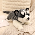 Realistic husky plush toy with soft black and white fur lying on a cozy knit blanket - Husky
