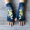 Blue knitted fingerless gloves with yellow flower embroidery on light wood background - Aqua