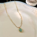 Macrodetail van ovale groene kattenoog-hanger aan een gouden roestvrijstalen ketting - Titanium staal/Kattenoog steen / Groen