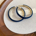 Dettaglio di orecchini a cerchio floccati blu scuro su sfondo di lino naturale e legno - Blu