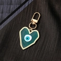Detail view of heart-shaped green resin keychain with a blue evil eye on dark fabric - Green Heart