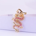 Llavero de dragón dorado con pedrería rosa y perla blanca sobre una caja de regalo - Rosa