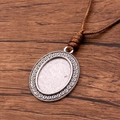 Antique silver oval pendant tray with brown braided cord on a textured wood surface - Spiral Pattern Oval Style