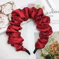 Cerchietto in raso plissettato rosso scuro con finitura lucida su sfondo decorativo - Borgogna
