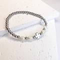 Detail view of silver beaded bracelet with freshwater pearls and a clover charm on white stone - Four-Leaf Clover / Steel