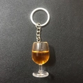 Close-up of a resin wine glass keychain with amber liquid on black leather texture - Coffee