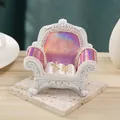 Golden X-shaped earrings with faux pearls displayed on a miniature pink sofa stand - Holographic Pink