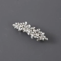 Dettaglio del fermaglio argento con cristalli a goccia su uno sfondo grigio neutro - Strass Argento