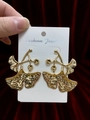 Detailed view of gold ginkgo leaf earrings held against a dark red velvet background - Shiny Gold Ginkgo Leaf Earrings