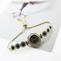 Macro view of gold quartz watch with floral diamond bezel and black stone bracelet - Gold Black