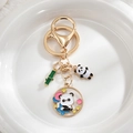 Detailed shot of golden panda keychain with bamboo charm on white ceramic display - Hugging Panda