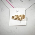 Detail of a golden alloy hair clip with wavy brushed texture on a marble background - Brushed Gold