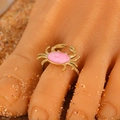 Adjustable gold crab toe ring with pink resin stone inlay on sandy beach background - Pink Crab (4731) / Gold