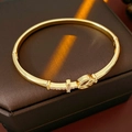 Detail van de gouden kruisarmband met kleine roze kristallen op luxe satijnen ondergrond - Goud (Echt Goud Verguld)