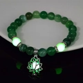 Macro shot of luminous lotus flower charm and green glow beads on a yoga bracelet - 8mm Natural Green Agate with Green Light