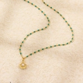 Gold shell pearl necklace featuring green enamel beads on a textured knit background - Gold