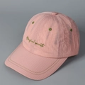 Close-up of pink plaid baseball cap featuring green Magical secrets cursive embroidery - Pink