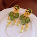 Detail view of vintage gold earrings with green gemstones on embossed ceramic plate - Silver Earring Post-Green