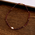 Close-up of red beaded necklace with freshwater pearl pendant on dark wood tray - Necklace / Red