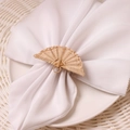 Handwoven fan-shaped bamboo napkin ring with white fabric napkin on ceramic plate - Fan