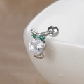Vue macro du piercing d'oreille hibou argenté avec zircons verts et pierre claire - Hibou / chouette