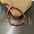 Close-up of red goldstone beaded bracelet with rectangular faceted beads on raw rock - Gold Sandstone