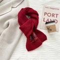 Detailed close-up of dark red wool knit scarf with embroidered bear patch and varsity text - Red