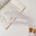 Close-up of a matte white large shark hair claw clip on an open book in a bright setting - 12.8cm / Matte White