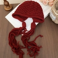 Dettaglio del berretto in maglia bordeaux con trama a rilievo e lunghe nappe decorative - Cappello in maglia con paraorecchie e nappe / Rosso