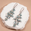 Detail of vintage heart-shaped teal zircon drop earrings on a white stone background - Blue